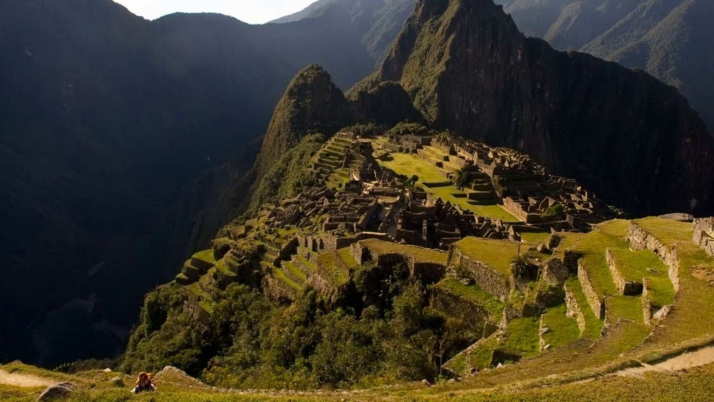 Modern mountain lodge with floor-to-ceiling windows overlooking misty Machu Picchu peaks, featuring stone facade and lush gardens