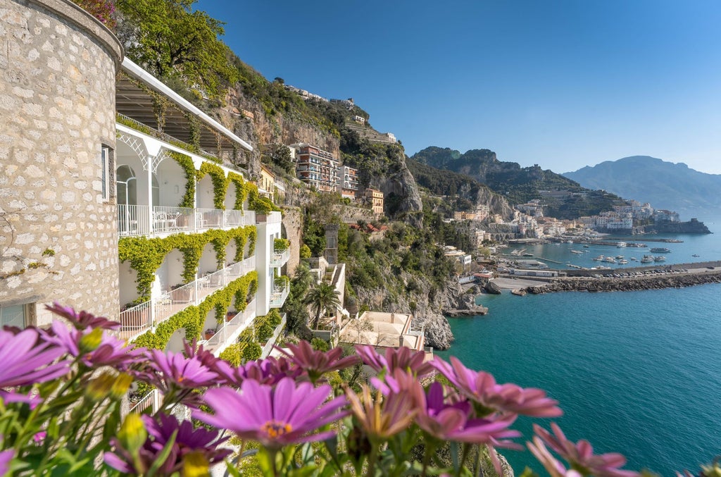 Elegant cliffside hotel with infinity pool overlooking the Amalfi Coast; white terraces cascade down mountain towards blue Mediterranean Sea