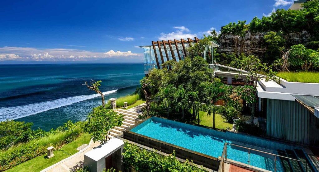 Luxury infinity pool overlooking lush Bali jungle at sunset, with curved wooden deck and elegant lounge chairs beside turquoise water