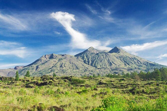 Sunrise hike on Mount Batur's volcanic terrain, showcasing misty peaks, lush greenery, and expansive Indonesian landscape at dawn's first light