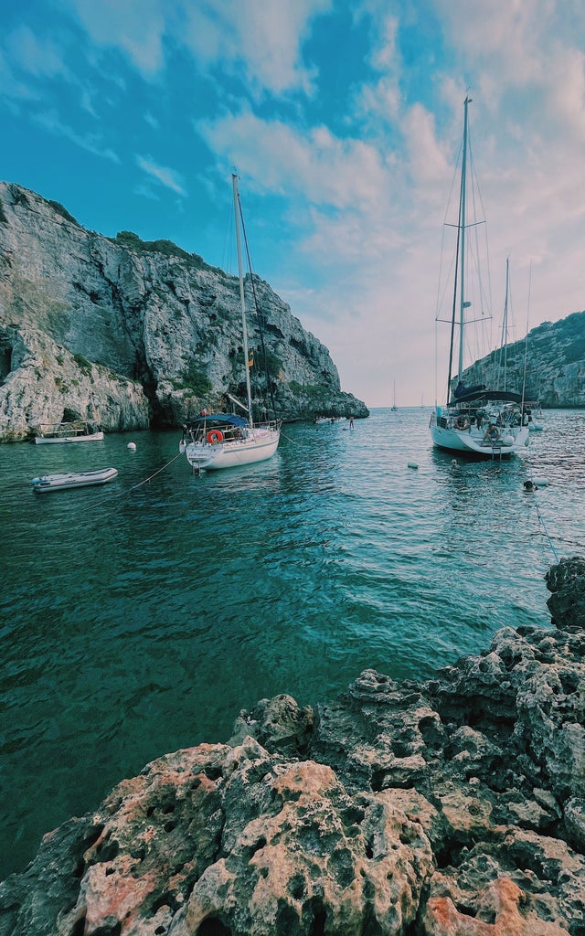 Luxurious yacht sailing along Menorca's turquoise coastline, passing white limestone cliffs and hidden coves under sunny skies