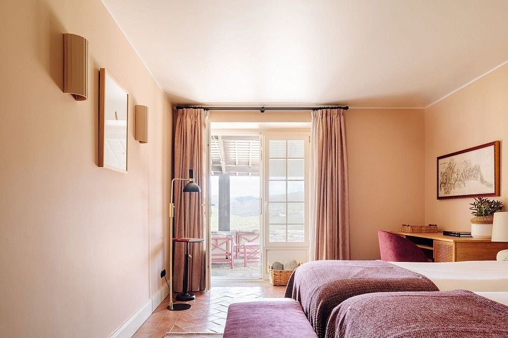 Modern hotel room with private terrace overlooking vineyard valley, featuring elegant white bedding and contemporary wood furnishings