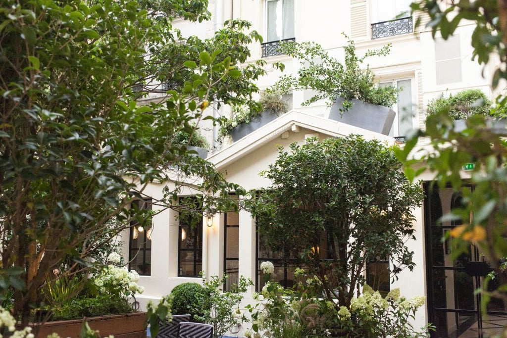 Elegant Parisian boutique hotel facade with soft pastel pink exterior, charming wrought-iron balconies, and delicate floral window treatments in a quaint neighborhood setting