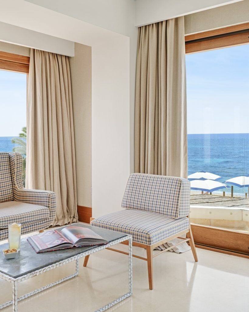 Luxurious loft-style hotel room with white decor, wooden accents, and large windows overlooking a scenic coastal landscape in Spain.