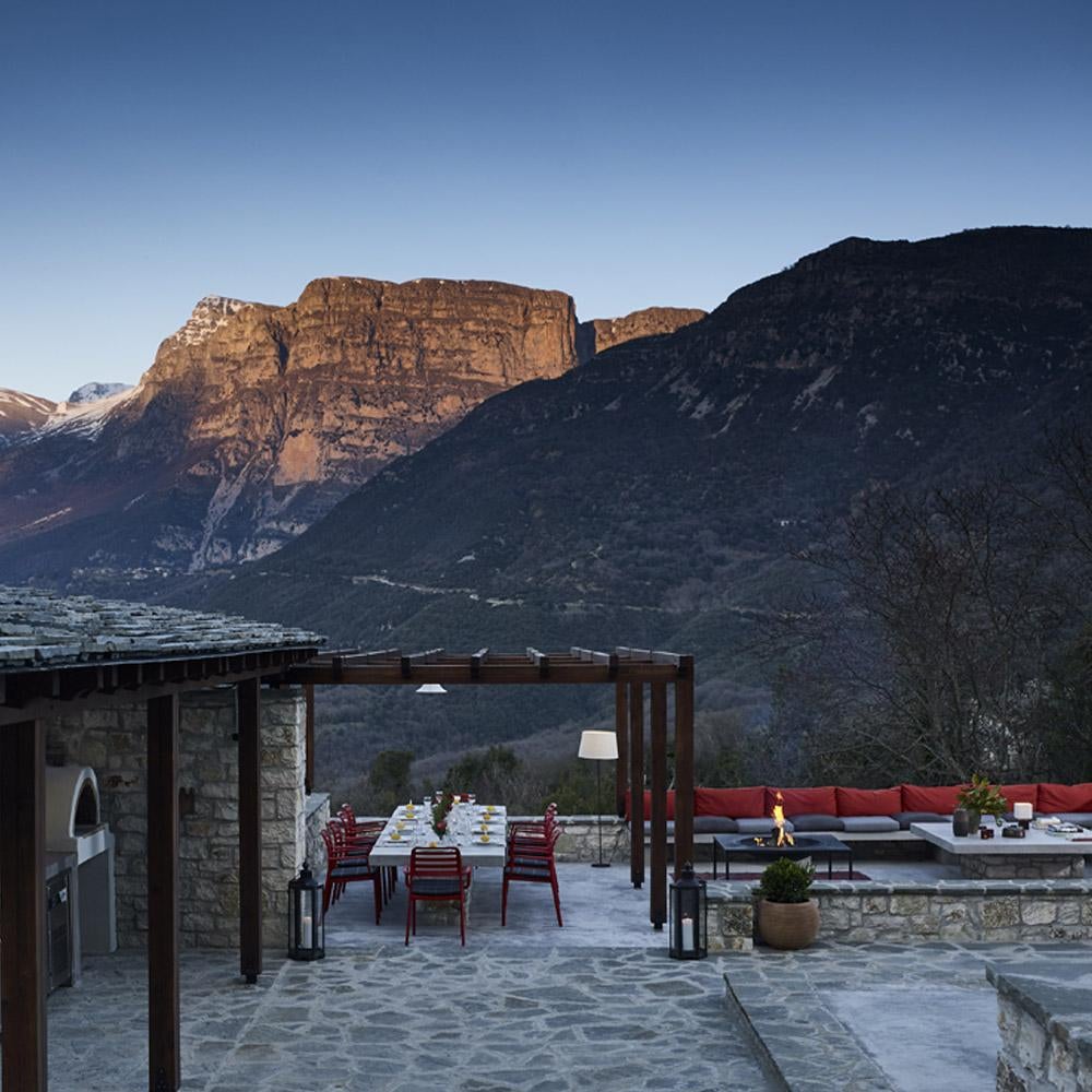 Stone-built luxury mountain resort with terraces nestled in misty Greek peaks, featuring traditional architecture and panoramic valley views