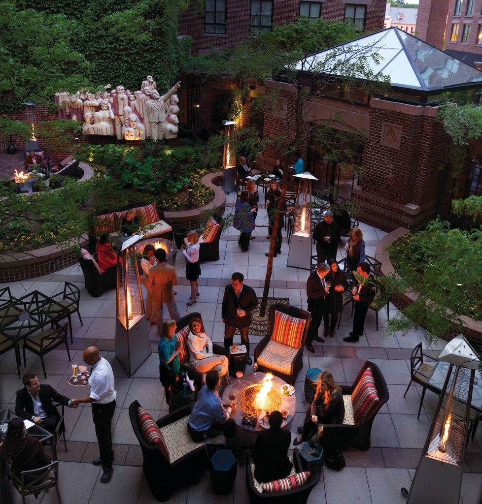 Elegant stone facade of Four Seasons DC hotel featuring floor-to-ceiling windows, iron balconies, and manicured landscaping at dusk