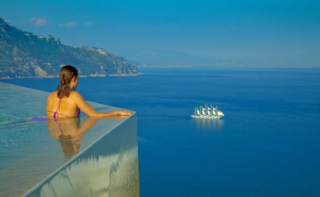 Cliffside luxury hotel overlooking Amalfi Coast, featuring infinity pool, stone walls, terraced gardens and Mediterranean Sea views