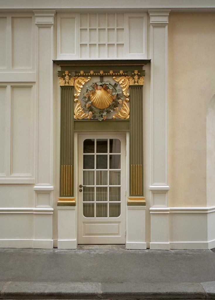 Elegant Parisian boutique hotel with Art Nouveau facade, soft cream walls, black iron balconies, and lush green window boxes in historic district