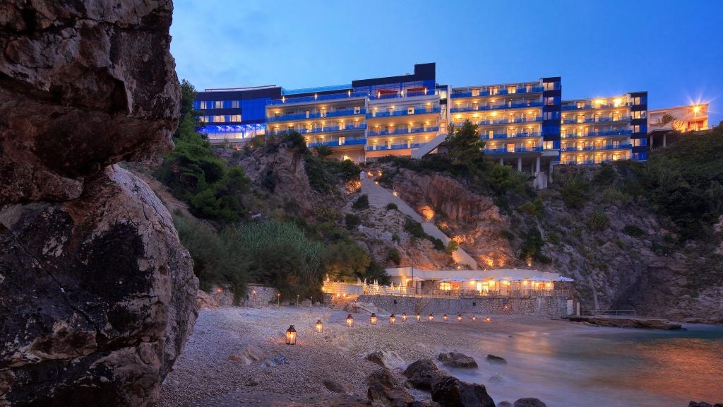 Sleek, cliffside luxury hotel with glass-front balconies overlooking the Adriatic Sea, nestled in Dubrovnik's rocky coastline