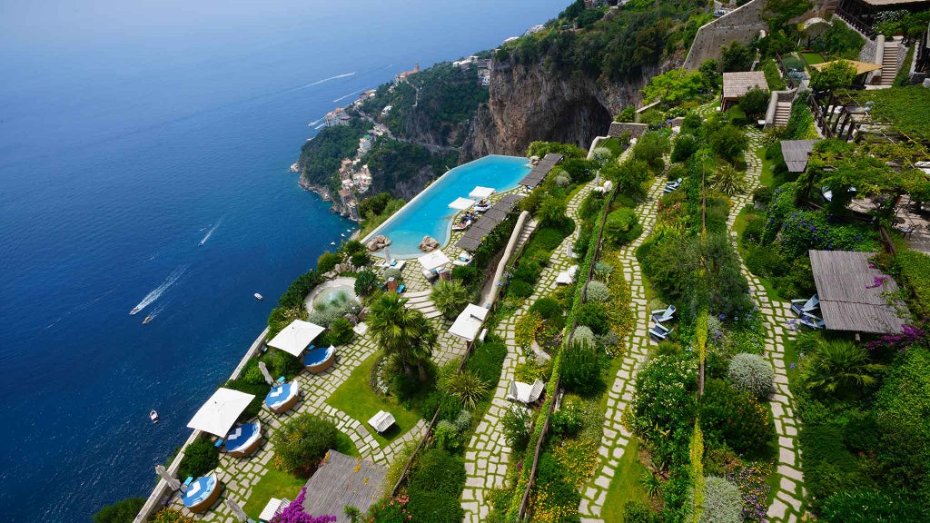 Luxury cliffside hotel with infinity pool overlooking Amalfi Coast, Mediterranean Sea and mountains at golden sunset hour