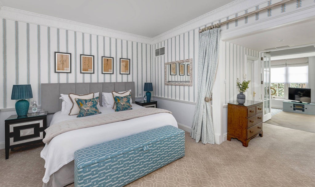 Elegant junior suite with soft beige tones, plush king bed, ornate period furnishings, and large windows overlooking historic Bath's architectural landscape