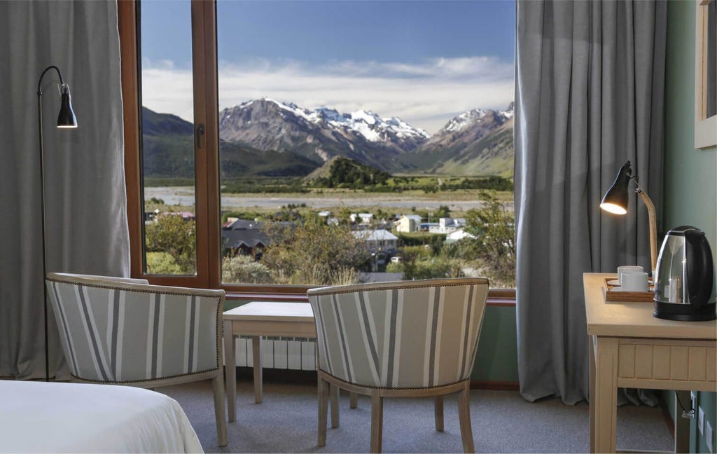 Elegant superior hotel room with wooden floors, plush white bedding, natural light, and mountain view at Los Cerros Boutique Hotel in Argentina