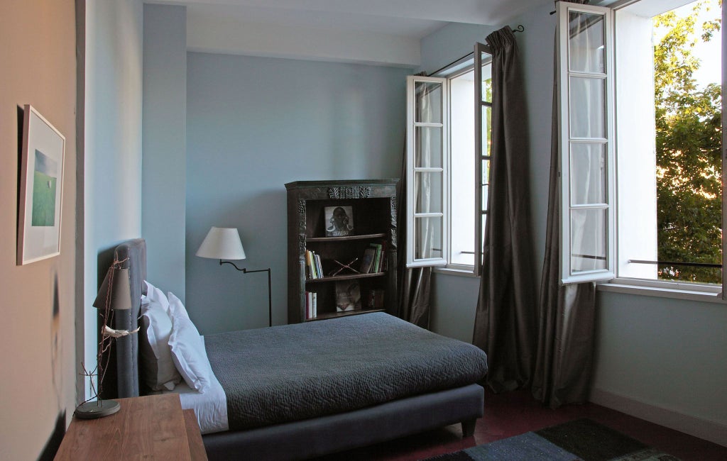 Luxurious French hotel suite with soft neutral tones, elegant canopy bed, antique wooden furniture, and delicate light filtering through ornate windows overlooking scenic landscape