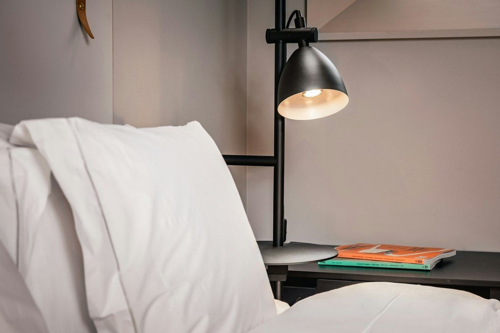 Contemporary minimalist hotel room with sleek gray furnishings, crisp white bedding, floor-to-ceiling windows, and elegant Scandinavian design in Stockholm's Blique by Nobis hotel