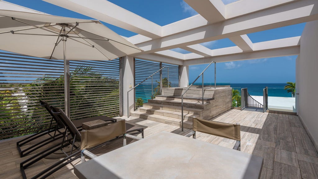 Elegant rooftop suite with infinity pool overlooking turquoise Caribbean waters, modern lounge chairs and private terrace at sunset