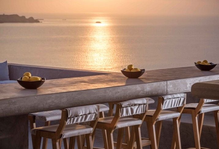 Luxury beachfront hotel with whitewashed walls and blue accents overlooking crystal waters of Aegean Sea at sunset in Mykonos, Greece