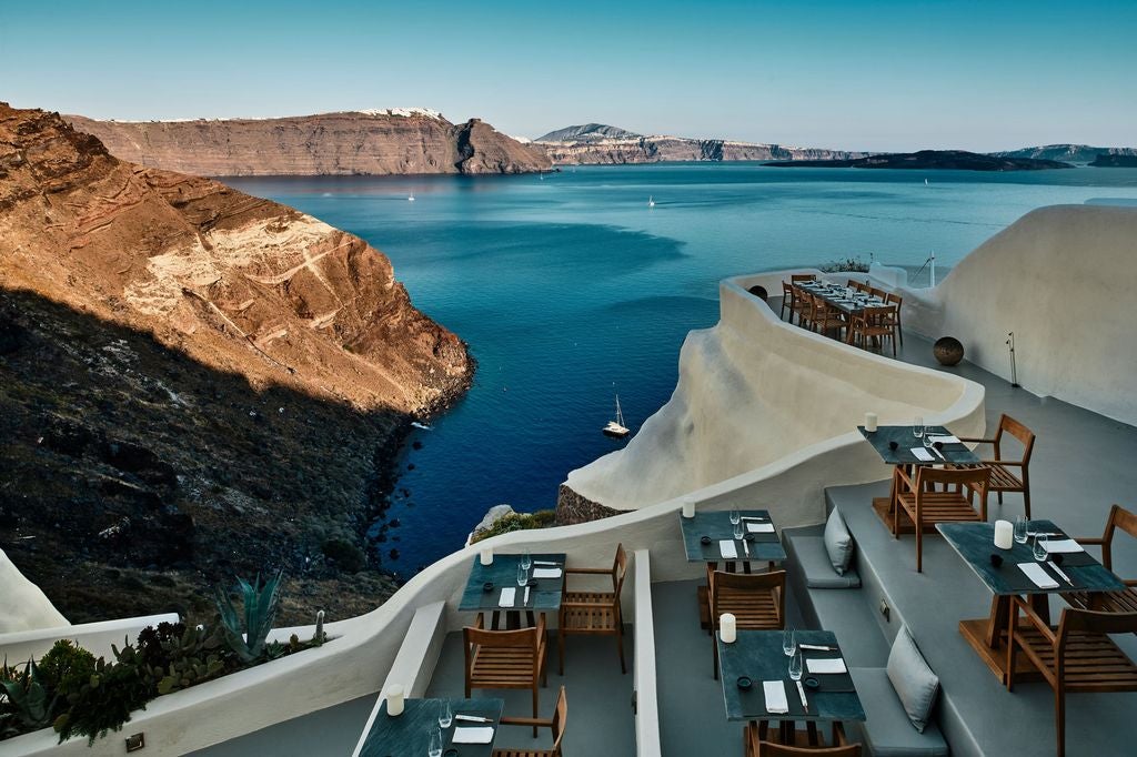 Whitewashed luxury cliffside suites with blue-domed roofs overlooking Aegean Sea, nestled into Santorini's dramatic caldera at sunset