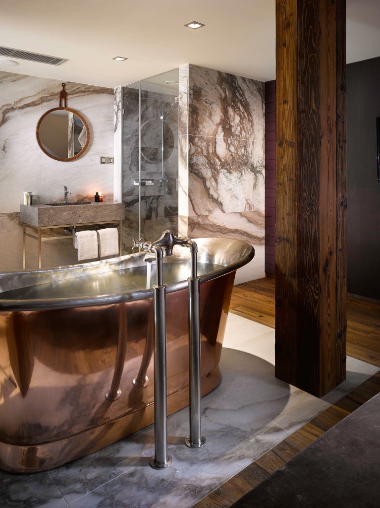 Luxurious library suite with dark wood shelves, elegant leather armchair, warm lighting, and sophisticated Czech design at The Emblem Hotel in Prague