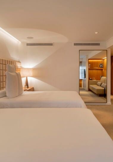 Elegant twin deluxe hotel room with modern Brazilian design, featuring sleek minimalist decor, crisp white linens, and sophisticated neutral color palette