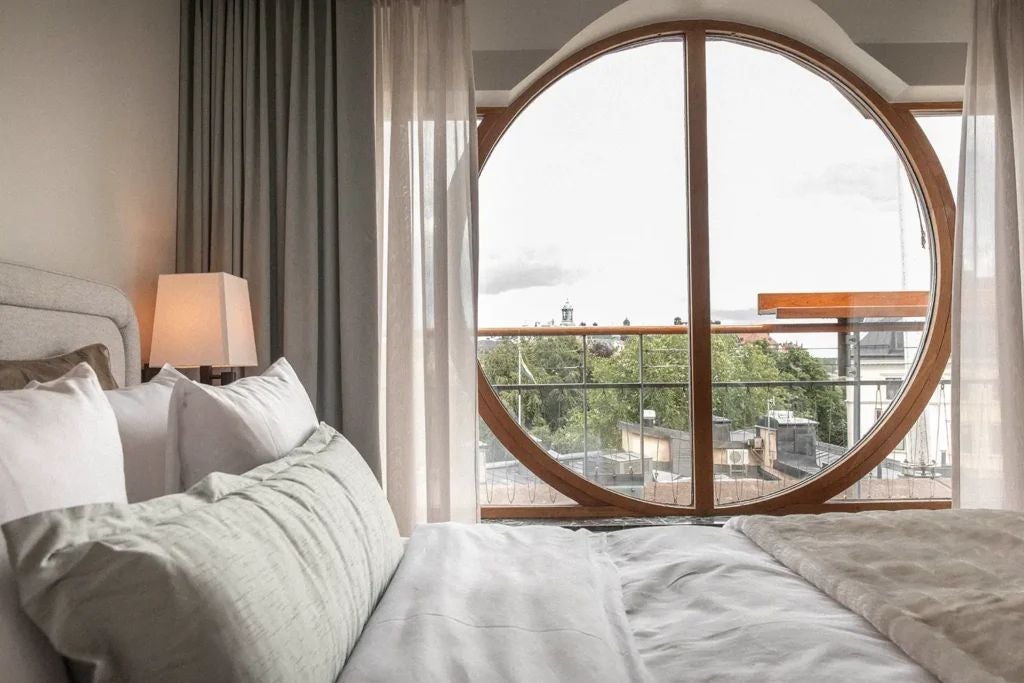 Elegant balcony suite with modern Swedish design, featuring panoramic city views, plush white bedding, and sleek contemporary furnishings in warm neutral tones