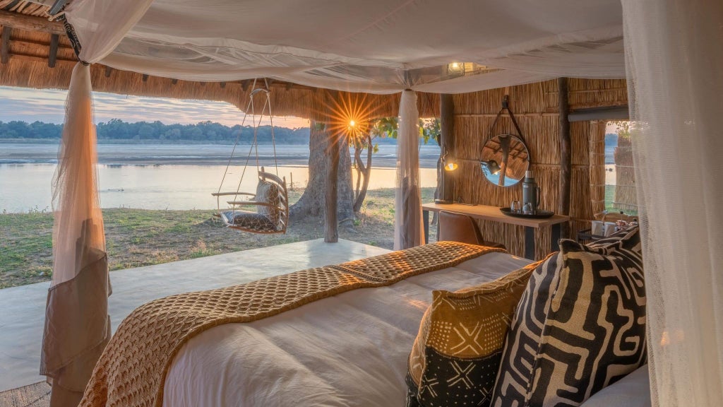 Luxurious safari lodge nestled in remote Zambian wilderness, featuring elegant canvas tents with wooden decks overlooking pristine riverine landscape