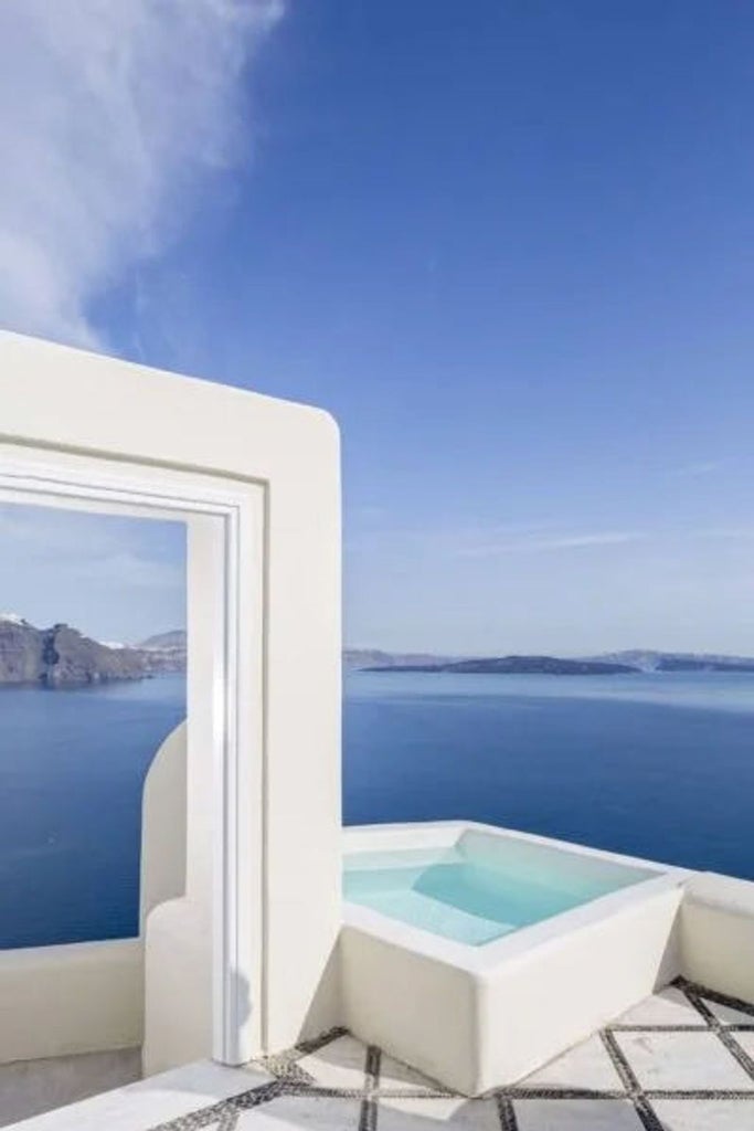 Elegant white-washed suite with private infinity pool overlooking Santorini's caldera and Aegean Sea during golden sunset hour