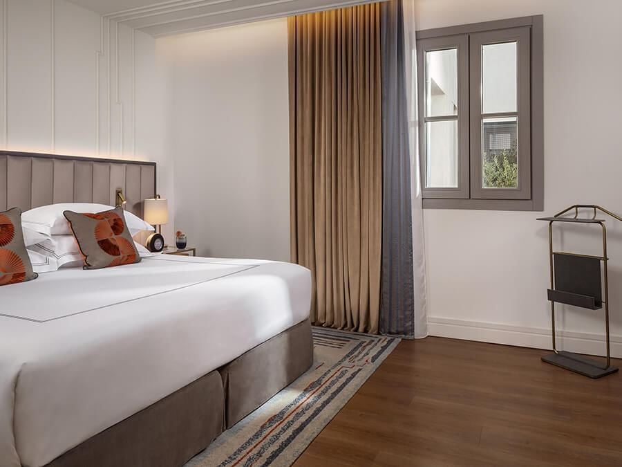 Elegant deluxe room at Gran Hotel Inglés with plush king bed, rich wooden furnishings, and soft neutral color palette in historic Spanish hotel setting