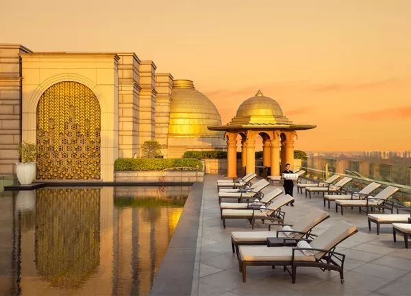 Luxurious exterior of a grand hotel with elegant architecture, marble columns, and lush landscaping against a dramatic sky in New Delhi, India