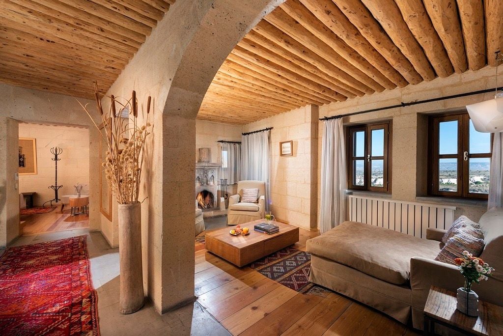 Elegant stone-walled junior suite at Argos in Cappadocia, featuring plush bedding, arched windows, and traditional Turkish architectural elements