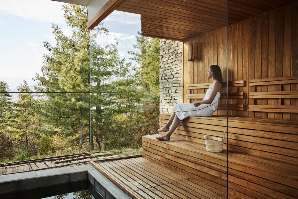 Stone and timber mountain lodge with floor-to-ceiling windows nestled on Bhutanese hillside, overlooking misty Paro Valley