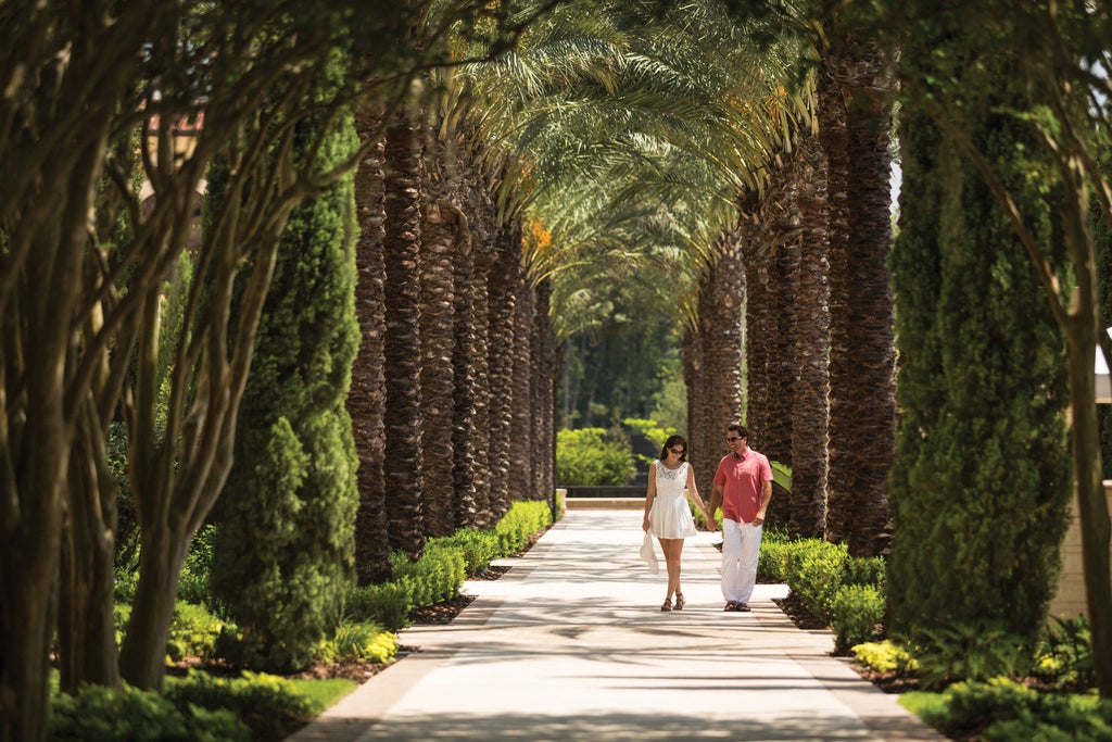 Opulent Mediterranean-style Four Seasons Orlando resort with palm-lined driveway, grand archways, and terracotta roofs at golden hour