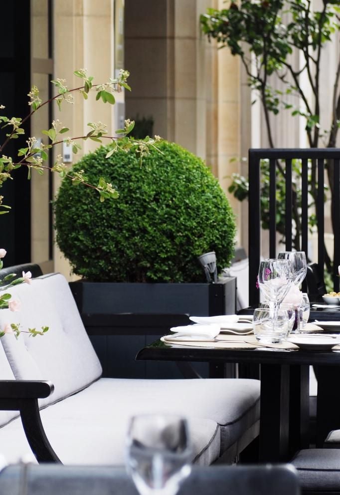 Elegant Parisian hotel exterior with classic French architecture, soft beige facade, wrought-iron balconies, and chic street-level entryway along a sophisticated urban boulevard