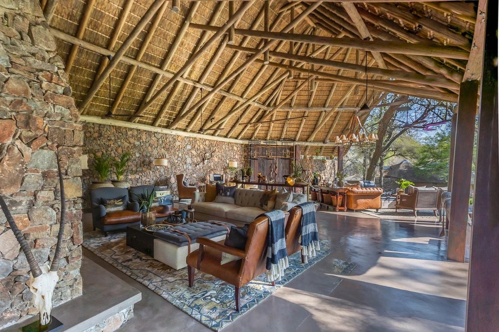 Elegant safari lodge with thatched roof and expansive wooden deck overlooking a serene waterhole in the African bush at sunset