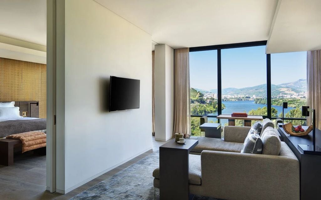 Luxurious suite with floor-to-ceiling windows overlooking Douro Valley vineyards, modern wood furnishings and private terrace seating