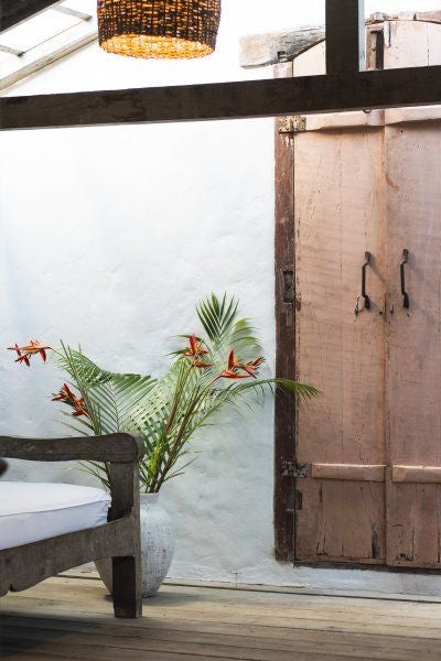 Luxurious rustic Brazilian hotel room with wooden furnishings, elegant white linens, and tropical greenery at UXUA Casa Hotel and Spa in Trancoso