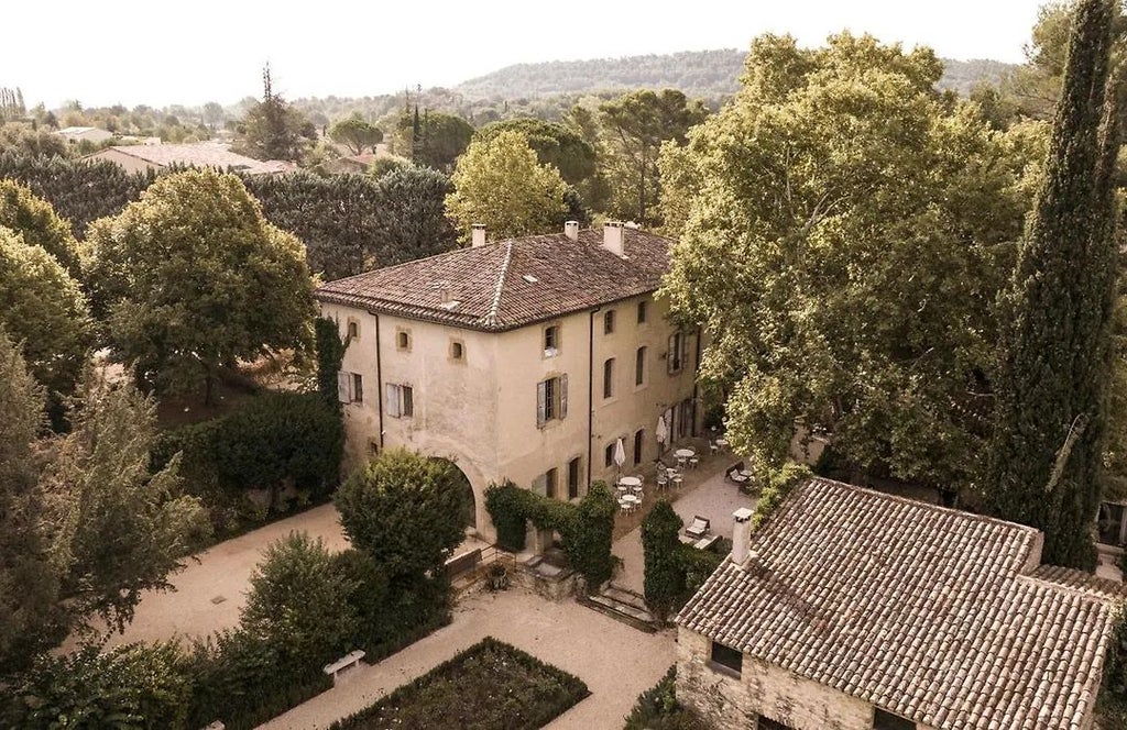 Elegant stone facade of Le Galinier hotel in Provence, with warm terracotta roof, lush lavender garden, and inviting stone terrace under soft sunlight