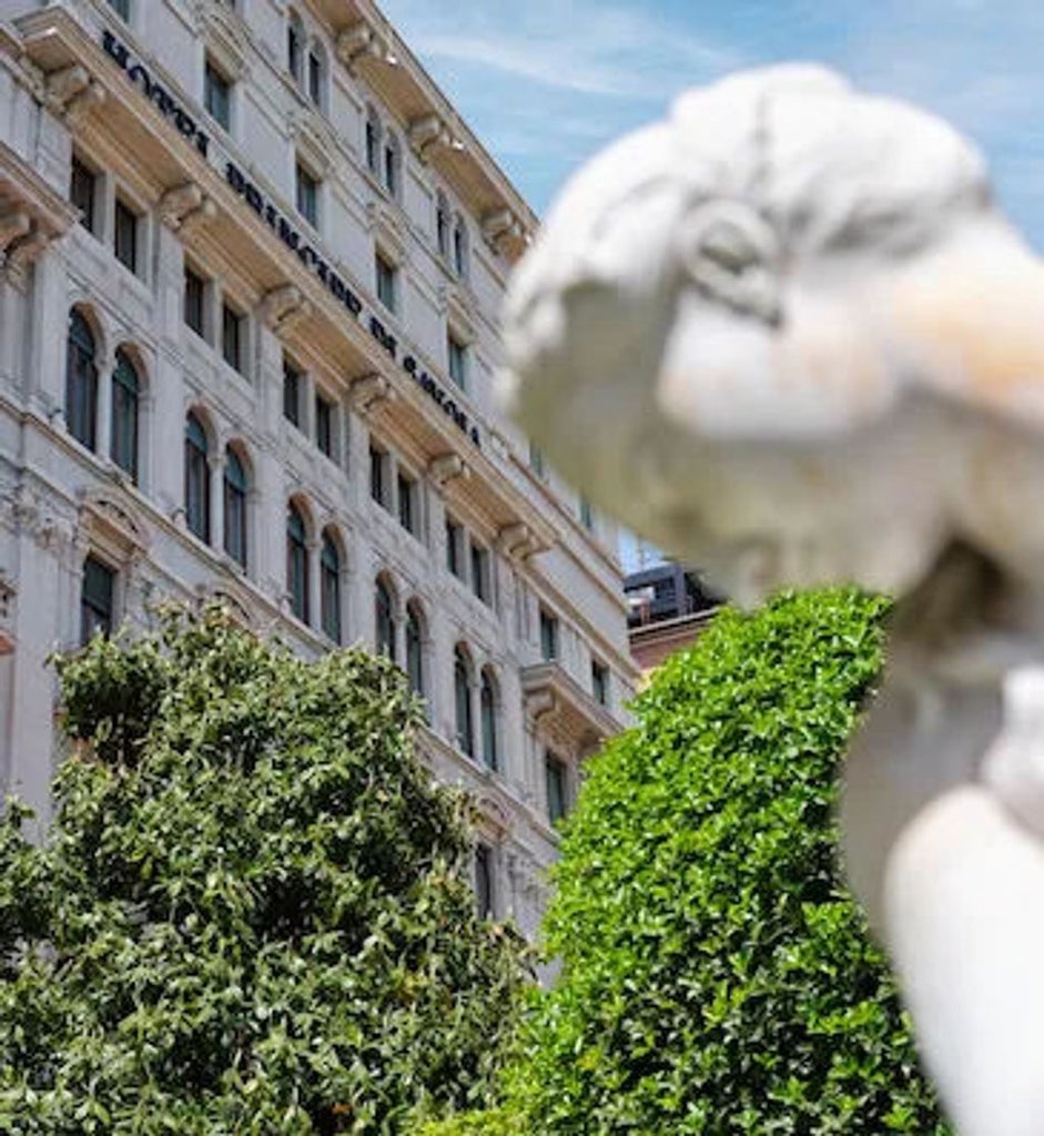 Elegant Italian neoclassical hotel exterior with ornate stone balconies, tall arched windows, and manicured hedges along its facade