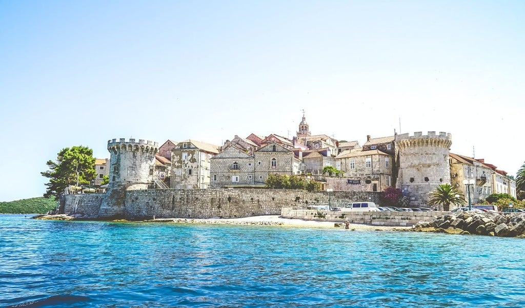 Historic stone buildings with red-tiled roofs line the Adriatic waterfront of Korčula, a medieval Croatian town nestled on a peninsula