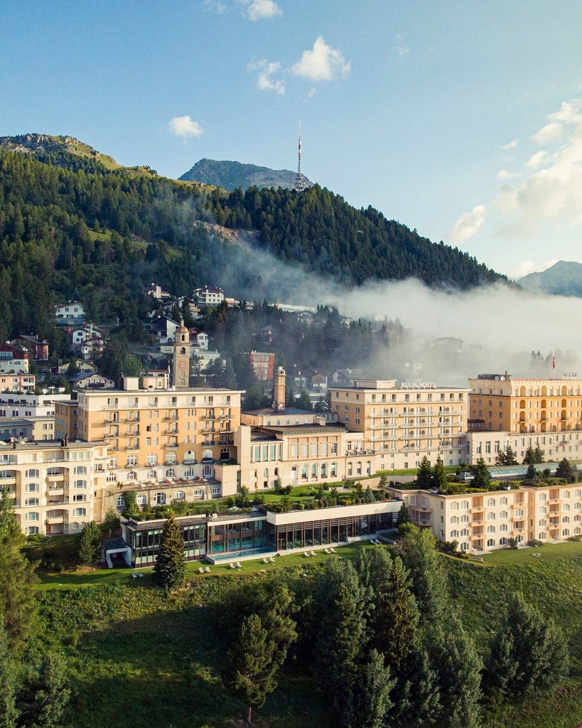 Luxurious alpine hotel with stone facade and classic Swiss architecture nestled against snowy mountains, overlooking Lake St. Moritz