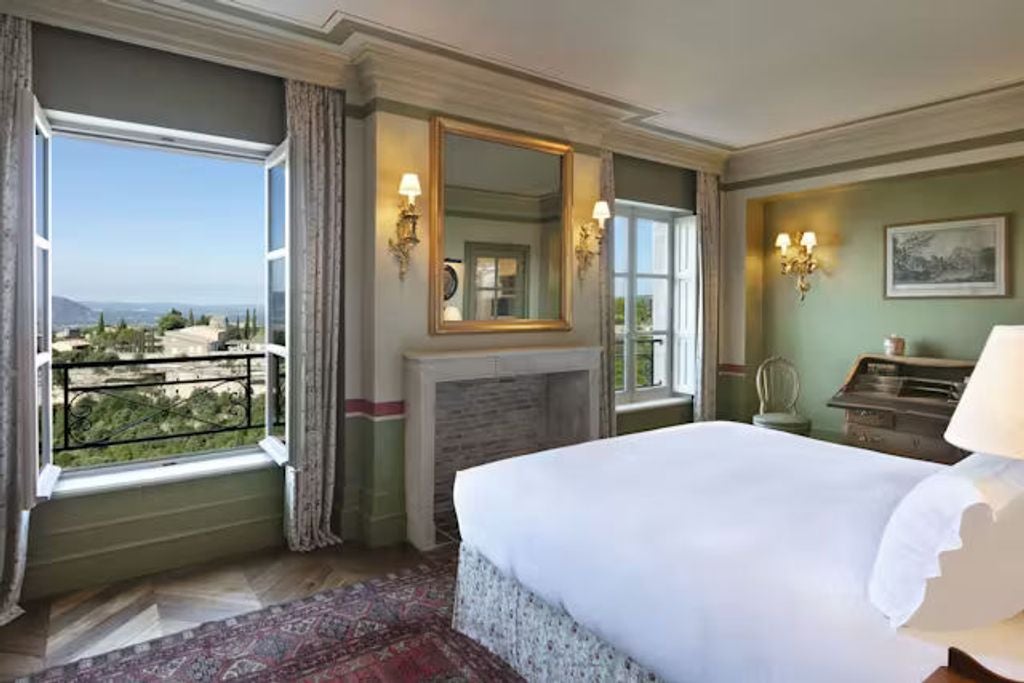 Elegant junior suite with king bed, crystal chandelier, exposed stone walls, and French windows overlooking Provence countryside