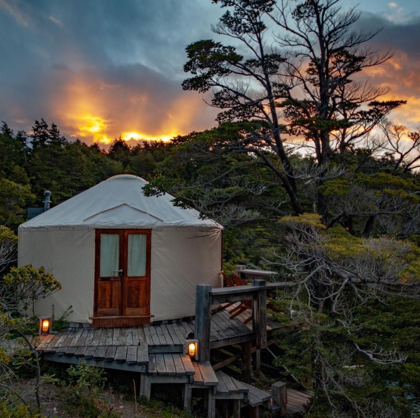 Luxury domed tent cabin at Patagonia Camp nestled in forest, with wooden deck overlooking pristine mountain lake at sunset