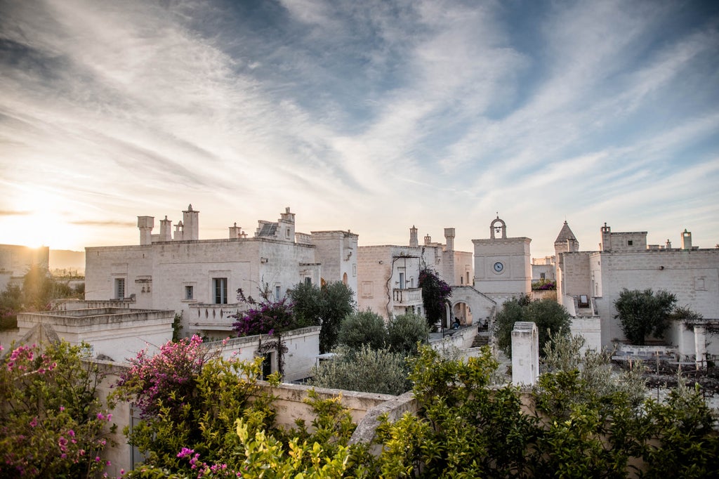 Elegant Mediterranean resort with white stone buildings, grand archways and lush gardens beneath a sunset sky in Puglia, Italy