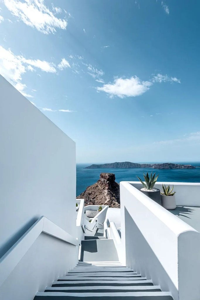 Whitewashed luxury villa with infinity pool overlooking Santorini's caldera at sunset, featuring curved architecture and ocean views