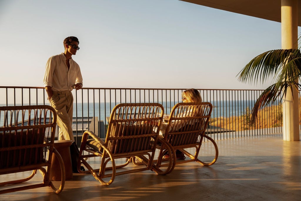 A luxury beachfront resort with sleek black buildings, infinity pools, and modern sun loungers overlooking the Mediterranean Sea at sunset