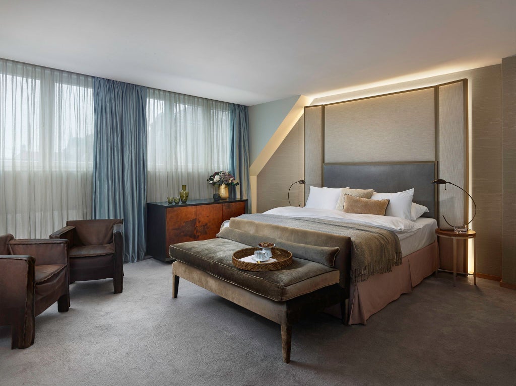 Elegant suite with plush king bed, marble-accented bathroom, panoramic Prague city views, and sophisticated contemporary design in soft neutral tones