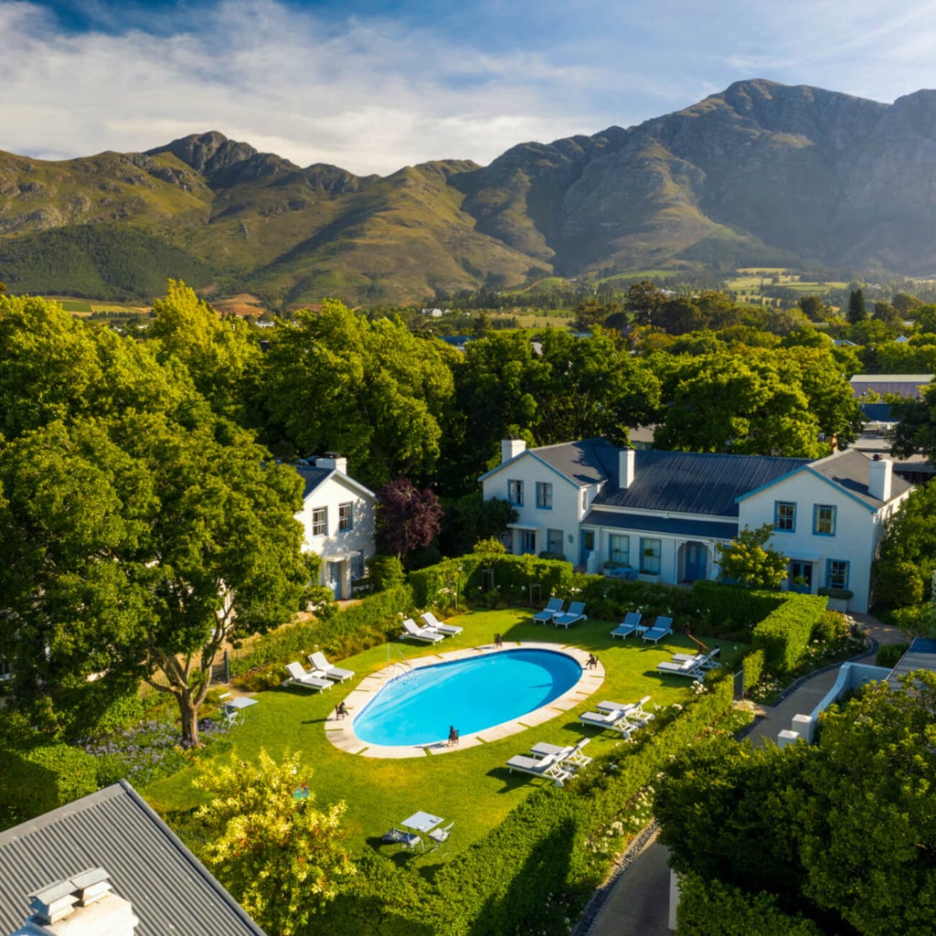 Elegant white-washed boutique hotel in Franschhoek, South Africa, with manicured gardens, French colonial architecture and mountain backdrop