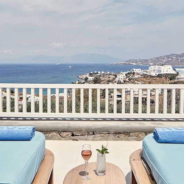 Luxurious white-walled Sunset suite with panoramic Aegean Sea view, minimalist design, private balcony, and elegant Mykonos architectural elements at dusk