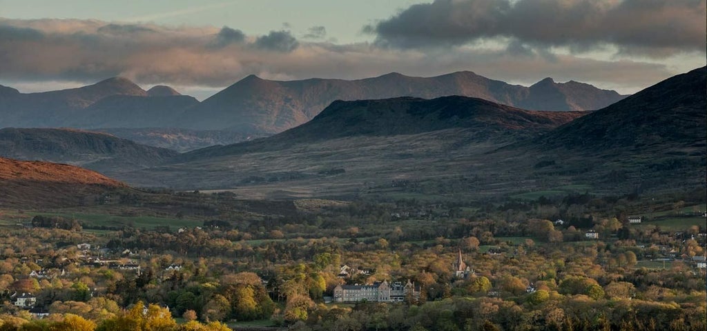 Elegant luxury hotel nestled in lush Irish countryside, featuring stone facade, manicured gardens, and mountain backdrop near scenset Kerry landscape