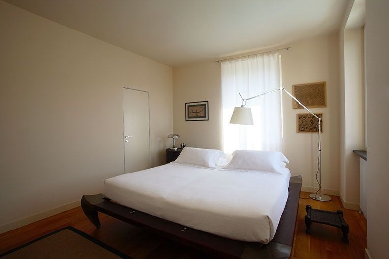 Elegant Italian villa guest room with soft cream walls, rosemary-green accents, king bed, and panoramic window overlooking Tuscan countryside landscape