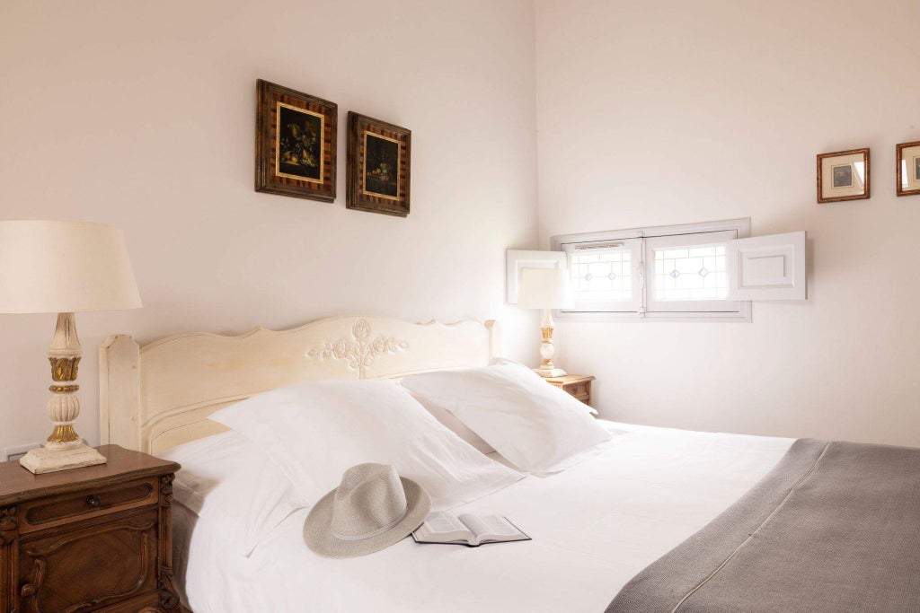 Elegant stone-walled hotel room with plush white linens, antique wooden furniture, and soft natural light filtering through rustic French windows